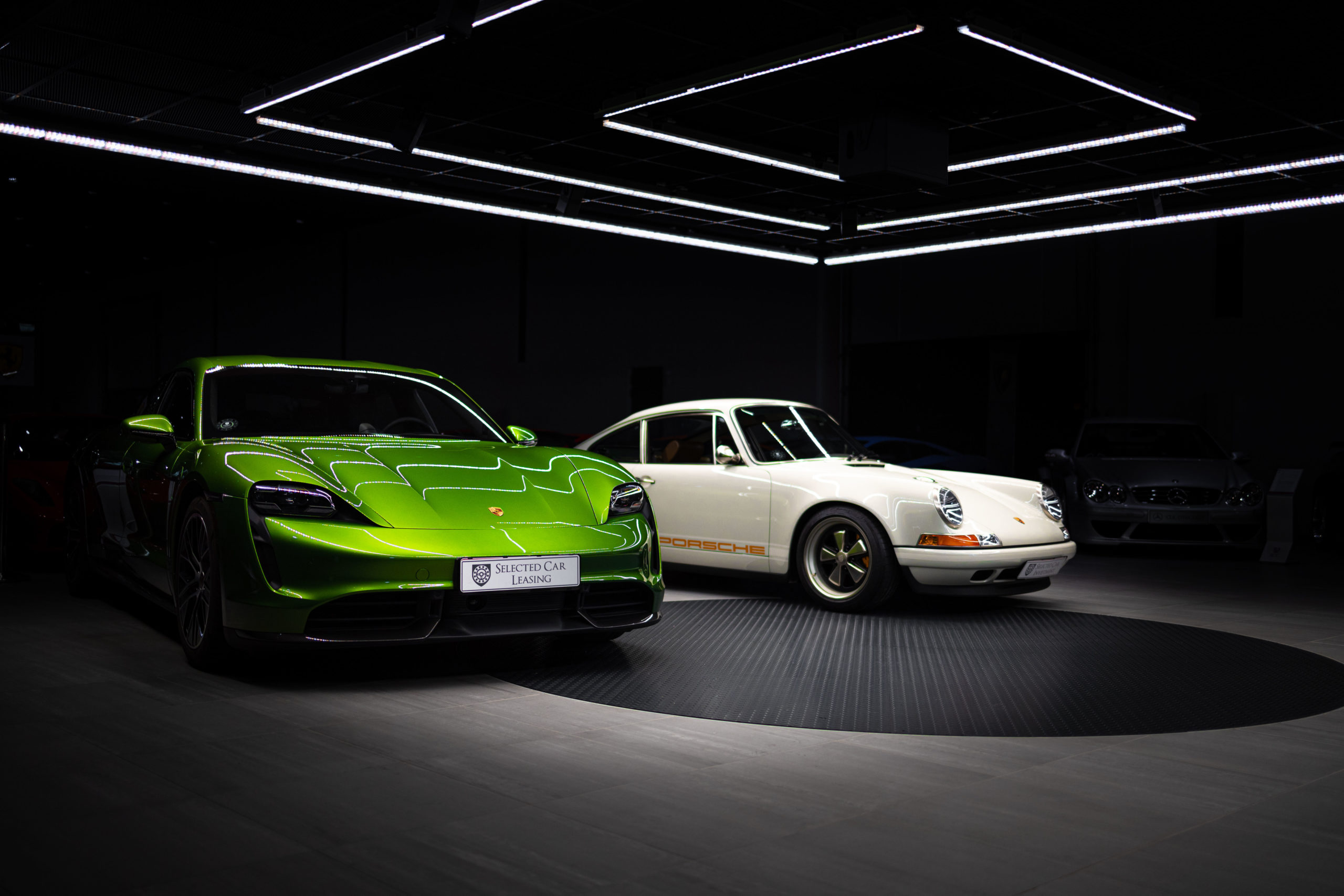 Grøn Porsche Taycan og klassisk hvid Porsche 911 i showroom – Selected Car Group